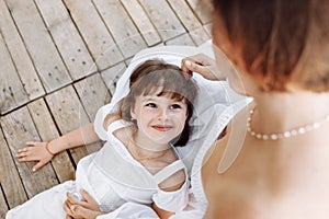 Happy young mom and child girl sitting near lake, pond. Mother and daughter smiling while spending free time outdoors