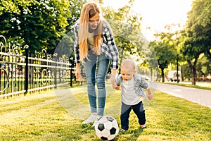 Happy young mom and her little son play soccer together outdoors
