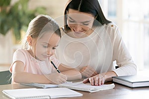 Happy young mom and little daughter study at home