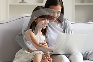 Happy young mom and little daughter using laptop at home