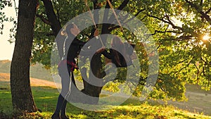 Happy young mom with a little girl swinging in the park together at sunset. Mother and daughter riding on swing, family
