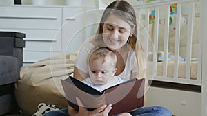 Happy young mother with baby boy reading big book on floor at living