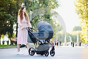 Happy young mother with baby in buggy walking in autumn park