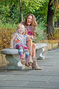 Happy young mother and baby girl talking mobile phone in city park