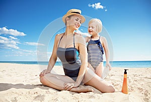 Happy young mother and child on beach applying sun screen