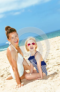 Happy young mother and child in beachwear sitting on seacoast