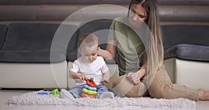 Happy young mother and child boy play together with pyramid indoors at home. Mom and baby toddler playing and having fun