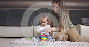 Happy young mother and child boy play together with pyramid indoors at home. Mom and baby toddler playing and having fun