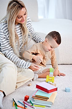 Happy young mother and child playing game with toys at home together, on floor.