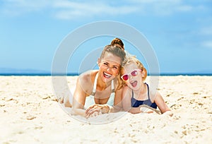 Happy young mother and child in swimsuit laying on seacoast