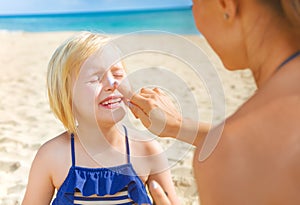 Happy young mother and daughter on beach applying SPF