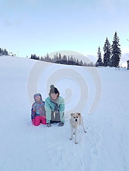 Happy young mother with daughter in the winter park with dog.