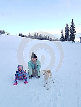 Happy young mother with daughter in the winter park with dog.