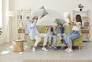 Happy young mother, father and children having a pillow fight on sofa in living room