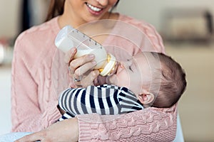 Happy young mother feeding her baby son with feeding bottle at home