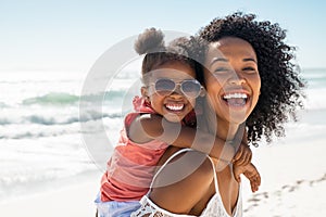 Happy young mother giving laughing daughter piggyback ride at beach