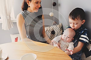 Happy young mother having breakfast in modern kitchen with her baby daughter and kid son