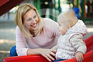 Happy young mother with her baby boy playing in colorful playground for kids