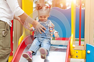 Happy young mother with her baby girl playing in colorful playground for kids. Mom with toddler having fun at summer park.