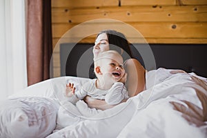 Happy young mother and her baby playing in bed.