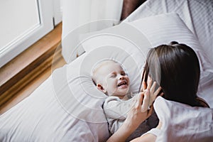 Happy young mother and her baby playing in bed.