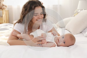 Happy young mother with her cute baby on bed at home