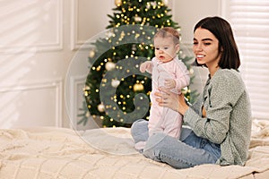 Happy young mother with her cute baby on bed at home, space for text. Winter holiday