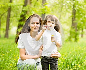 Happy young mother and her daughter blowing soap bubbles in park