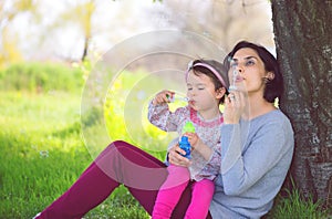 Happy young mother and her daughter blowing soap bubbles