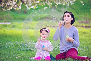 Happy young mother and her daughter blowing soap bubbles