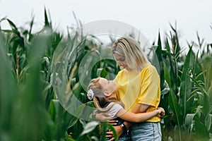Happy young mother and her daughter in a corn field hug and look at each other