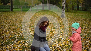 Happy Young Mother and her Little Daughter Having Fun in an Autumn Park, Mom and Girl Throwing Leaves and Laughing. slow