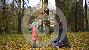 Happy Young Mother and her Little Daughter Having Fun in an Autumn Park, Mom and Girl Throwing Leaves and Laughing. slow