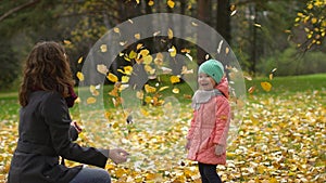 Happy Young Mother and her Little Daughter Having Fun in an Autumn Park, Mom and Girl Throwing Leaves and Laughing. slow