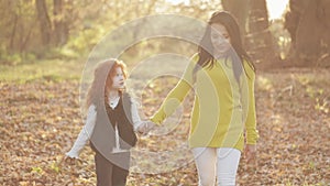 Happy young mother and her little redhead daughter walking together in an autumn park. They laughing and having fun