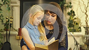 Happy young mother with her little smiling daughter reading the bood together - indoors