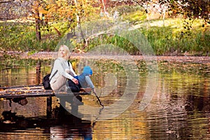 Happy young mother and her son spending time in the autumn park near the pond.