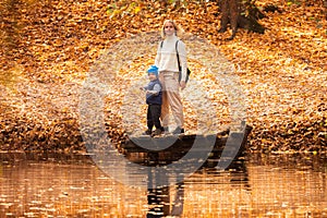 Happy young mother and her son spending time in the autumn park near the pond.