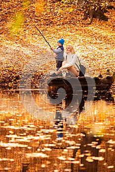 Happy young mother and her son spending time in the autumn park near the pond.