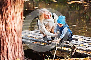 Happy young mother and her son spending time in the autumn park near the pond.