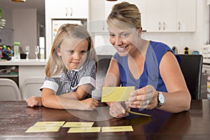 Happy young mother and her sweet and beautiful little daughter playing card game at home kitchen smiling and having fun together