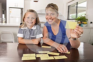 Happy young mother and her sweet and beautiful little daughter playing card game at home kitchen smiling and having fun together