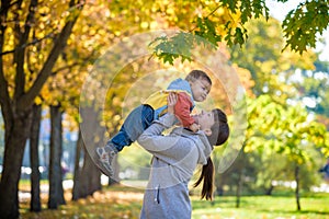 Happy young mother holding sweet toddler boy, family having fun together outside on a nice sunny autumn day. Cute adorable kid and