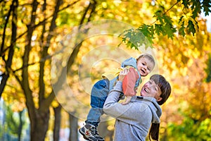 Happy young mother holding sweet toddler boy, family having fun together outside on a nice sunny autumn day. Cute adorable kid and