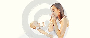 Happy young mother kissing feet her baby at home lying on the bed together on white background