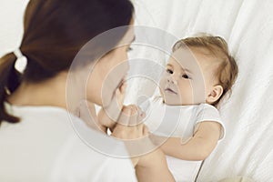 Happy young mother kissing her baby girl's little feet while cuddling on bed together