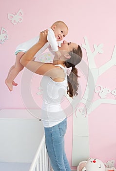 Happy young mother lifting cute baby out of crib