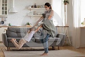 Happy mother lifting spinning child daughter dancing in modern kitchen