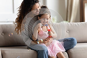 Happy young mother and little daughter blow soap bubbles