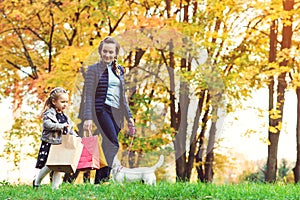 Happy young mother, little daughter with shopping bags. Autumn shopping, sales concept. Mom, daughter and their dog walking at aut